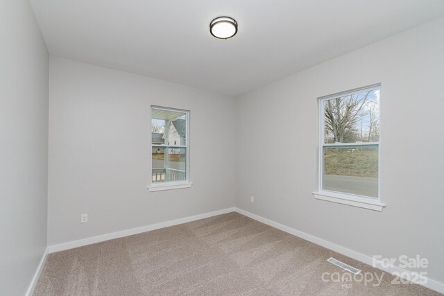 carpeted empty room with baseboards, visible vents, and a wealth of natural light