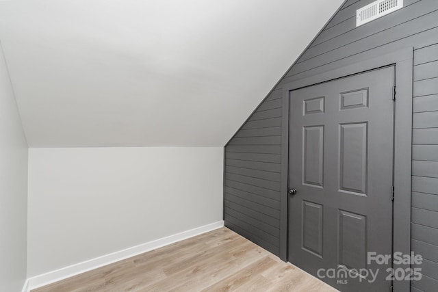 bonus room with light wood-type flooring, wood walls, baseboards, and lofted ceiling