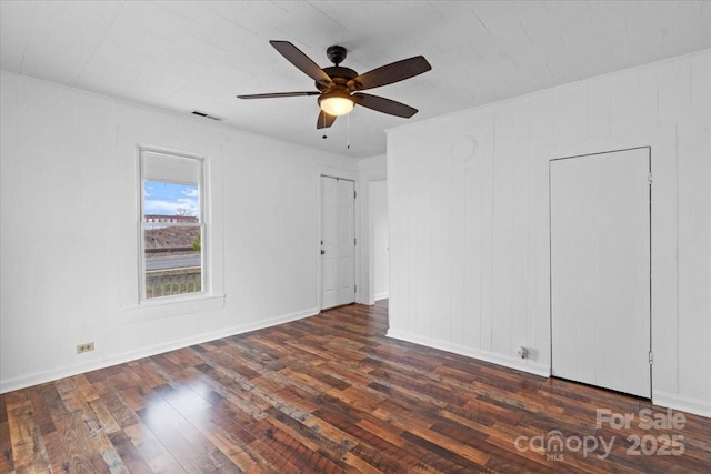 empty room with a ceiling fan, dark wood-style flooring, visible vents, and baseboards