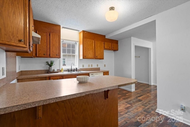 kitchen featuring brown cabinetry, a breakfast bar area, dark wood-style flooring, a peninsula, and a sink