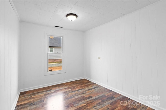 empty room with dark wood-style floors, visible vents, and baseboards