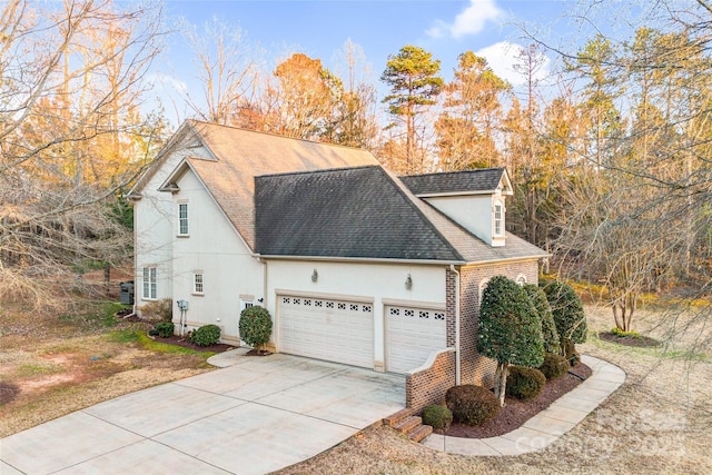 view of side of home with driveway, an attached garage, stucco siding, a shingled roof, and brick siding