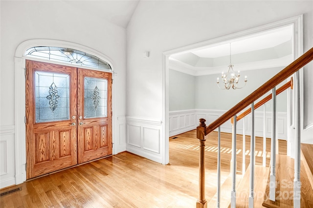 entrance foyer with visible vents, stairway, light wood-type flooring, wainscoting, and a notable chandelier