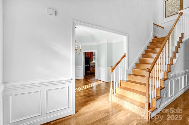 stairway with a chandelier, a decorative wall, crown molding, and wood finished floors