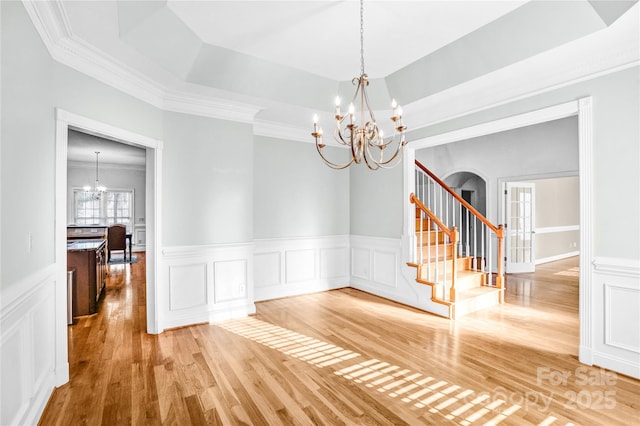 spare room featuring light wood-type flooring, stairs, a tray ceiling, arched walkways, and a notable chandelier