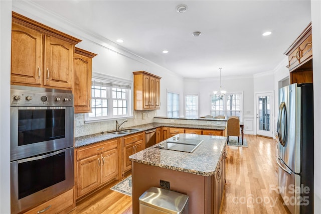 kitchen featuring a peninsula, ornamental molding, a sink, light wood-style floors, and appliances with stainless steel finishes