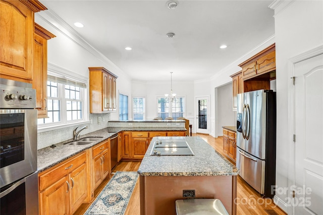 kitchen featuring light wood finished floors, a kitchen island, a peninsula, a sink, and appliances with stainless steel finishes