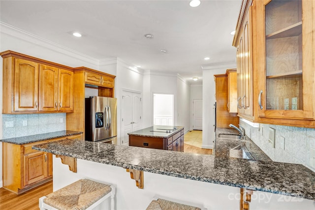 kitchen with dark stone counters, stainless steel fridge, glass insert cabinets, brown cabinets, and a center island