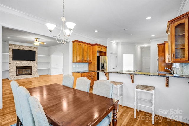 dining area with ceiling fan with notable chandelier, light wood-style flooring, a fireplace, and ornamental molding