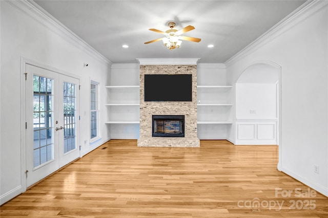 unfurnished living room featuring ornamental molding, built in features, wood finished floors, french doors, and a large fireplace