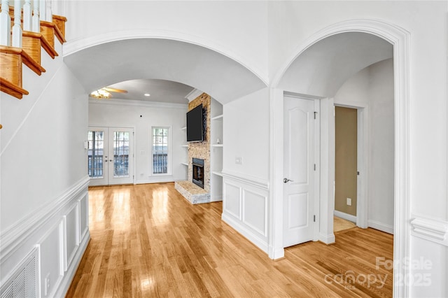 unfurnished living room with light wood finished floors, visible vents, a stone fireplace, french doors, and a decorative wall