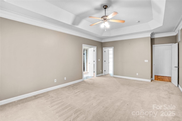 unfurnished bedroom with light carpet, ornamental molding, a ceiling fan, a tray ceiling, and baseboards