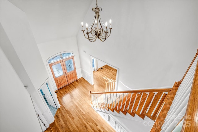 foyer featuring stairs, light wood-type flooring, a towering ceiling, and a chandelier