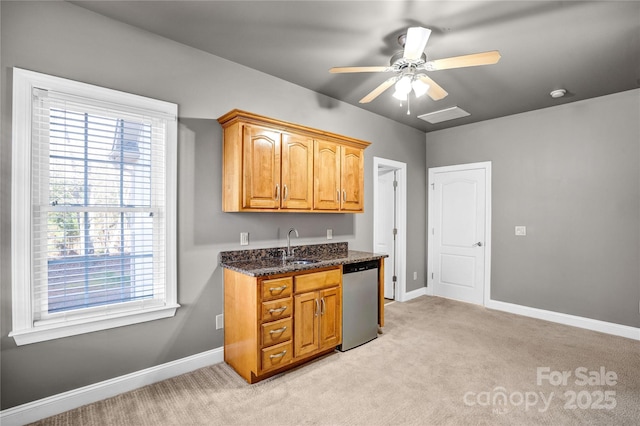 kitchen with stainless steel dishwasher, dark stone countertops, baseboards, and light carpet