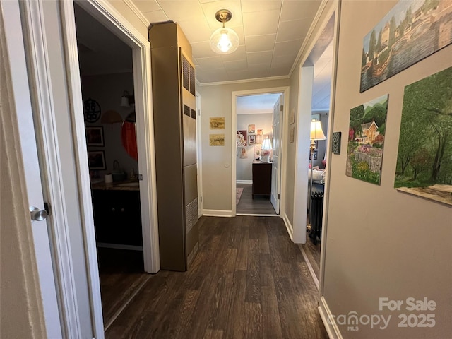 corridor with dark wood-style floors, crown molding, and baseboards