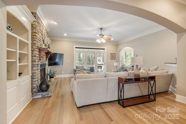 living room featuring arched walkways, a stone fireplace, light wood-style flooring, and ornamental molding