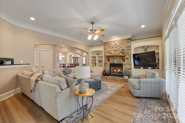 living room with built in features, wood finished floors, baseboards, arched walkways, and ornamental molding