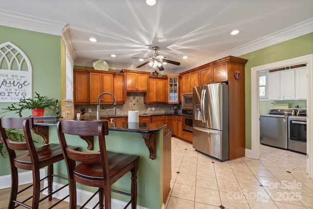 kitchen featuring dark countertops, washing machine and dryer, appliances with stainless steel finishes, a peninsula, and brown cabinetry