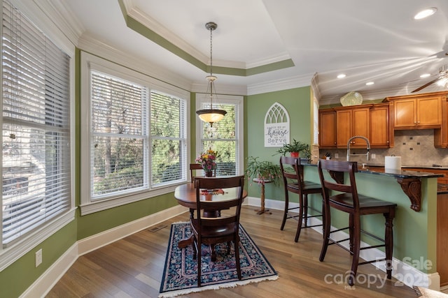 dining area with a raised ceiling, wood finished floors, baseboards, and ornamental molding