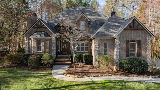 view of front facade with brick siding, a chimney, a front lawn, and roof with shingles