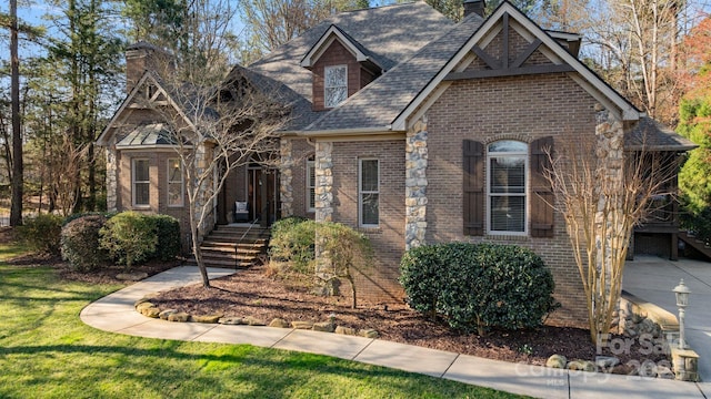 view of front of home with a front lawn, brick siding, a chimney, and a shingled roof