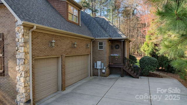 view of side of property with a garage, brick siding, roof with shingles, and driveway