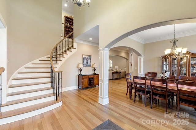 dining area with stairway, light wood finished floors, a high ceiling, arched walkways, and a chandelier