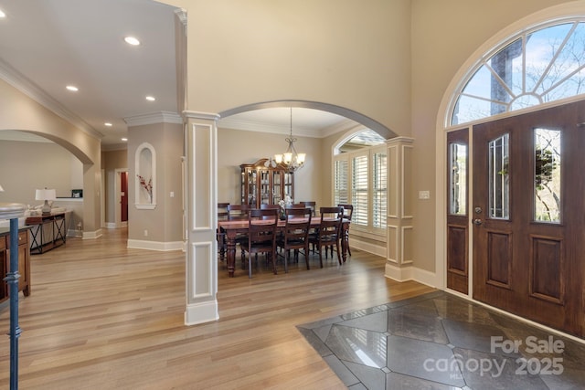 foyer entrance featuring baseboards, light wood-style floors, arched walkways, and a chandelier