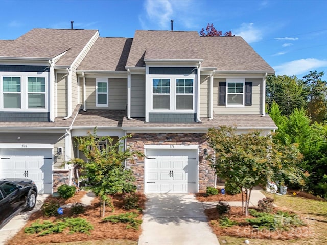 townhome / multi-family property with concrete driveway, stone siding, a shingled roof, and an attached garage