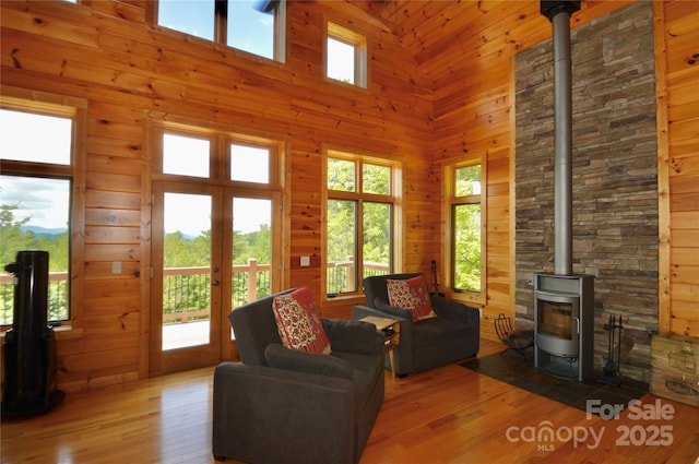 living room with wood-type flooring, a towering ceiling, a wood stove, and wooden walls