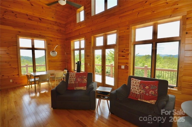 living area featuring french doors, wood-type flooring, a towering ceiling, a ceiling fan, and wooden walls