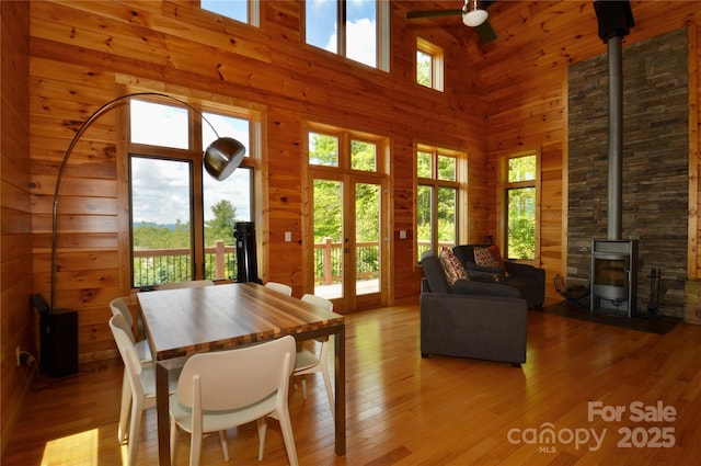 dining room with a wood stove, wood walls, light wood-style flooring, and a towering ceiling