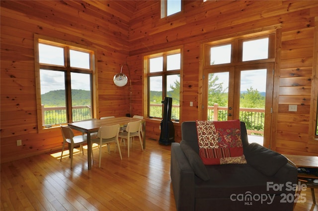 living room with french doors, a towering ceiling, light wood-style flooring, and wooden walls