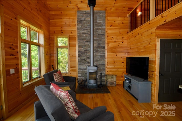 living area featuring wood walls, a towering ceiling, a wood stove, and light wood-style floors