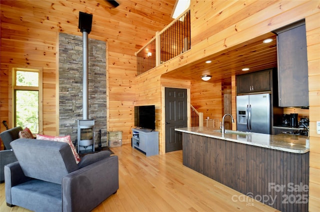 kitchen featuring open floor plan, a wood stove, wood walls, stainless steel refrigerator with ice dispenser, and a sink