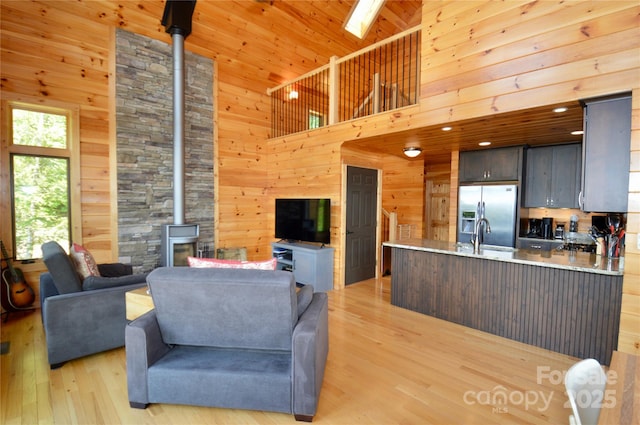 living room with light wood-style flooring, a wood stove, wooden walls, and a towering ceiling