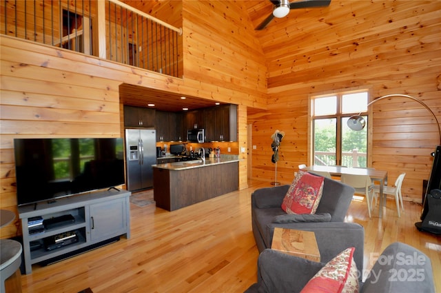 living room with light wood-style floors, high vaulted ceiling, wooden walls, and ceiling fan