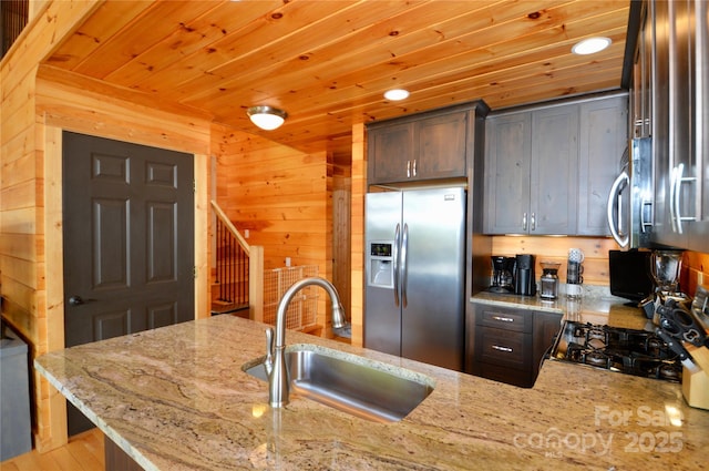 kitchen with appliances with stainless steel finishes, wooden ceiling, a sink, and light stone counters