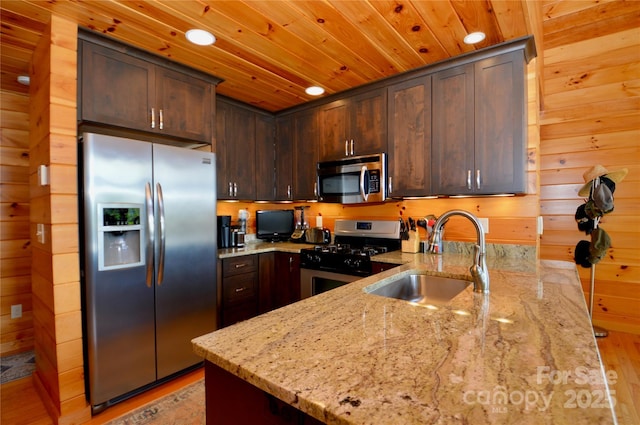 kitchen with wooden walls, wood ceiling, appliances with stainless steel finishes, light stone counters, and a sink