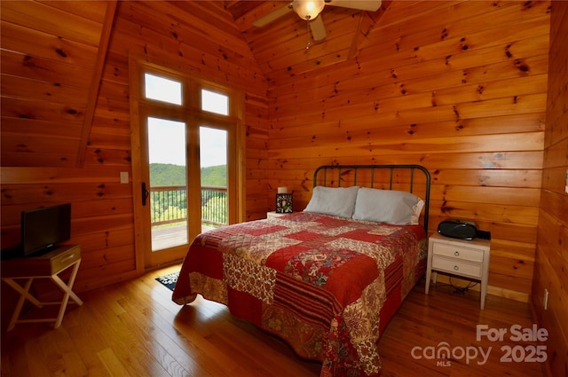 bedroom with lofted ceiling, access to exterior, wooden walls, and wood finished floors