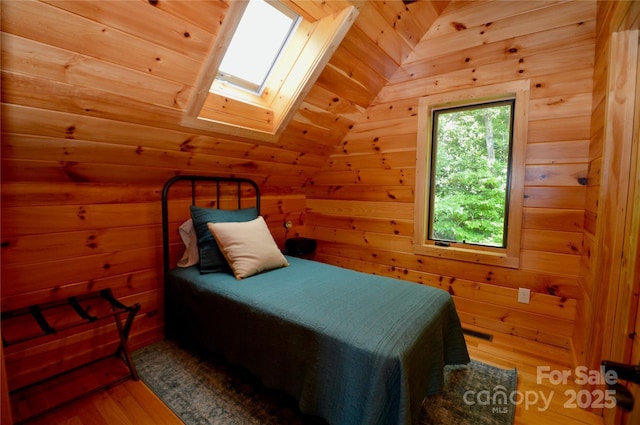 bedroom with lofted ceiling with skylight, wood walls, and wood finished floors