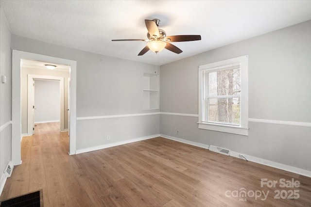 empty room featuring baseboards, visible vents, ceiling fan, and wood finished floors