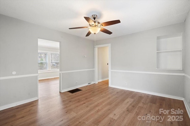 unfurnished room with visible vents, ceiling fan, baseboards, and wood finished floors