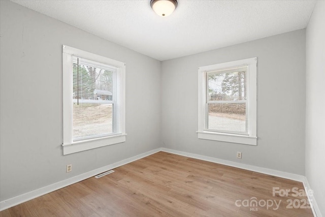 spare room with visible vents, plenty of natural light, baseboards, and wood finished floors