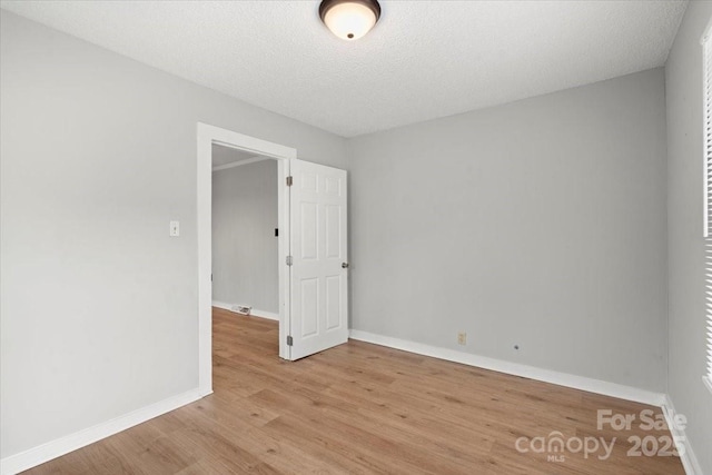 unfurnished room featuring a textured ceiling, light wood finished floors, visible vents, and baseboards