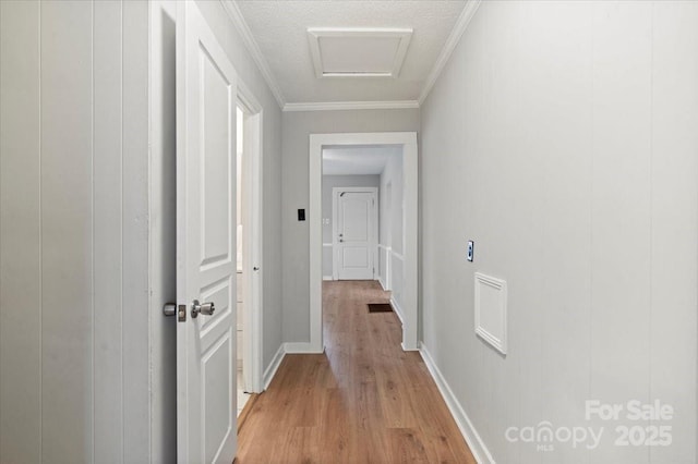 corridor featuring baseboards, light wood-type flooring, attic access, and crown molding