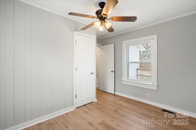 unfurnished bedroom with visible vents, baseboards, a ceiling fan, light wood-style flooring, and ornamental molding