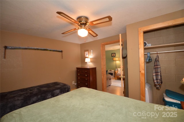 bedroom with ceiling fan, a closet, and concrete block wall