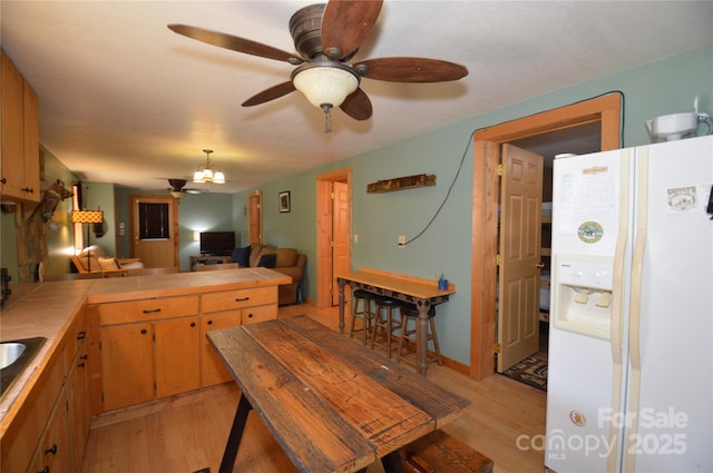 kitchen featuring tile countertops, a peninsula, light wood-style floors, open floor plan, and white fridge with ice dispenser