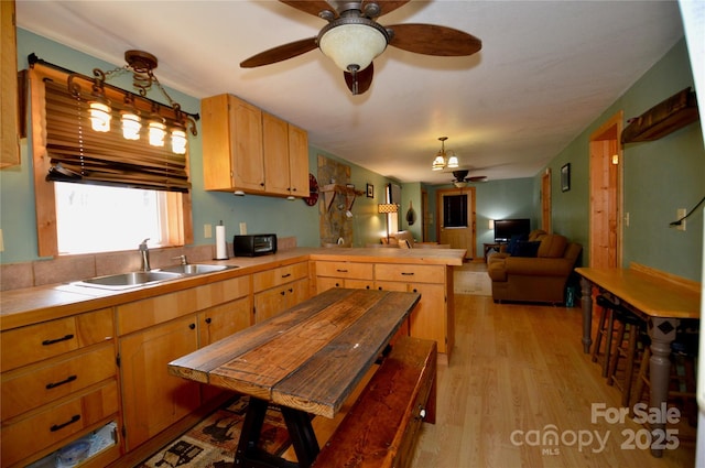 kitchen with light wood finished floors, tile counters, a ceiling fan, a sink, and a peninsula